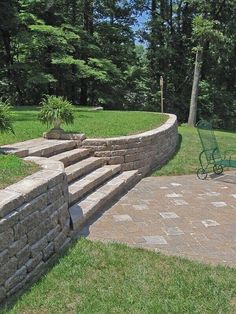 a green chair sitting on top of a stone walkway next to a lush green park