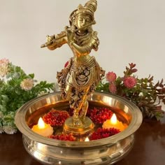 there is a small brass statue in the center of a bowl with candles around it