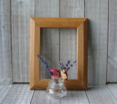 a small vase with flowers in it sitting next to a wooden frame on a table