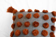 a gray and orange pillow with pom - poms on it