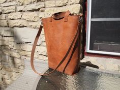 a brown leather bag sitting on top of a table next to a brick wall and window