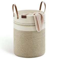 a white and brown basket with handles on the bottom, holding a blanket in it