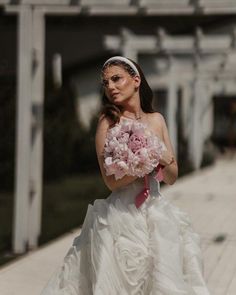 a woman in a white wedding dress holding a pink bouquet and looking at the camera