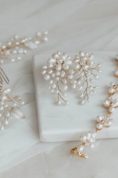 two pieces of jewelry sitting on top of a white cloth covered table next to each other