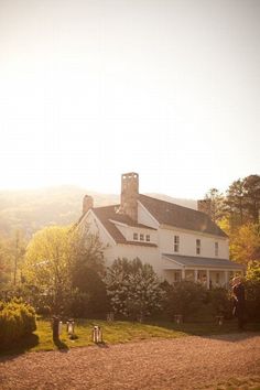 a large white house sitting in the middle of a lush green field next to trees