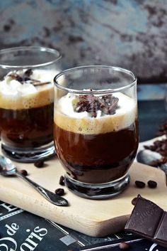 two glasses filled with dessert sitting on top of a cutting board next to chocolate chips