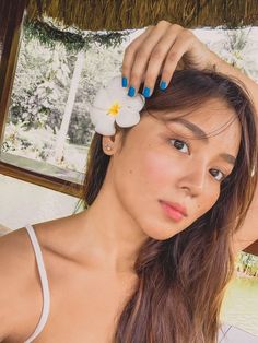 a woman with blue and white nail polish holding a flower in her hair while looking at the camera