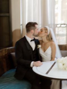 a bride and groom kissing in front of a table with flowers on it at their wedding