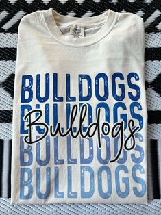 Get this popular new Bulldogs stacked text shirt and show off your school spirit in style!  Each shirt is printed in-house by me using high-quality materials on a Comfort Colors shirt, known for its exceptional comfort, style, and durability. Available in unisex sizes S to 3X, and youth sizes, we've got you covered regardless of your preferred fit. The Bulldogs stacked text Shirt features a classic crew neck and short sleeves, making it suitable for year-round wear. The flattering silhouette ensures a comfortable and stylish fit for both men and women. Please note that ivory is ONLY available in Adult sizes!  Note: As each shirt is individually printed, slight variations in color and placement may occur, adding to the uniqueness and charm of your Preppy Bulldogs Shirt. Your shirt will come Long Sleeve Cheer Shirts, Cheap School Spirit Shirt For Game Day, Bulldog Volleyball Shirts, Cheap Letter Print Tops For School Spirit, Middle School Spirit Wear, Cricut School Spirit Ideas, Sublimation School Spirit Shirts, College Cheer Shirts, Cheap School Spirit Shirt With Funny Text