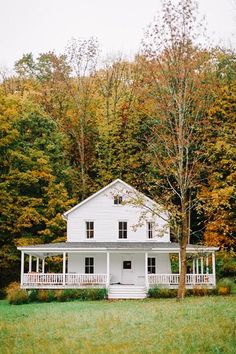 a large white house sitting in the middle of a lush green field next to trees