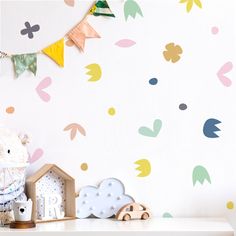 a teddy bear sitting on top of a white table next to a wall with colorful leaves