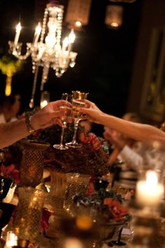 several people are toasting with wine glasses on a long table in front of chandeliers