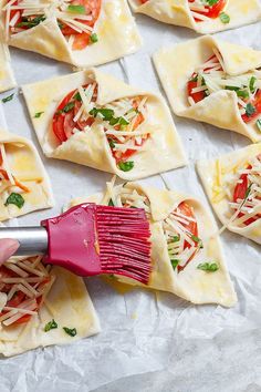 a hand holding a red brush over some ravioli with cheese and tomatoes on it