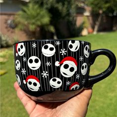 a hand holding a black coffee cup with skulls and snowflakes on it