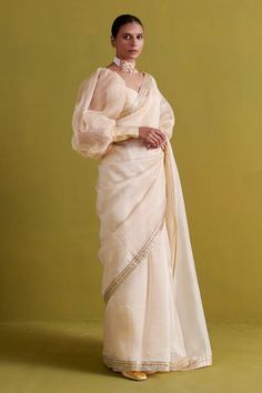 Beige saree in organza base hand embroidered with plumeria swirl border embroidery using gota patti and thread work. Paired with a bishop sleeves sweetheart neck raw silk blouse and shantoon petticoat. - Aza Fashions Party Organza Pre-draped Saree With Gota Work, Elegant Organza Blouse For Navratri, Fitted Organza Blouse Piece With Zari Work, Elegant Pre-draped Saree With Gota Work, Tissue Silk Blouse For Wedding And Eid, Elegant Organza Pre-draped Saree For Navratri, Bollywood Style Wedding Pre-draped Organza Saree, Semi-stitched Organza Blouse With Traditional Drape, Wedding Blouse In Tissue Silk With Resham Embroidery