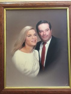 a man and woman are posing for a photo in front of a framed photograph on the wall