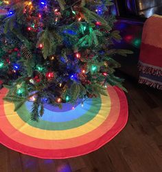 a brightly lit christmas tree sits in the middle of a living room with a rainbow rug on the floor