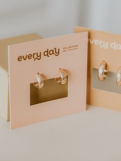 two pairs of earrings sitting on top of a card with the words every day written on it