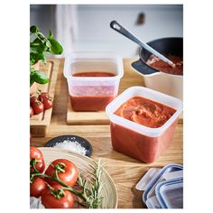 three containers of tomato sauce on a table with tomatoes and other food in the background