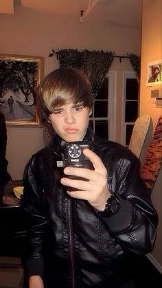 a boy in a black leather jacket holding a cell phone