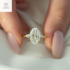 a woman's hand holding a diamond ring with two diamonds on the band and an oval shaped diamond in the middle