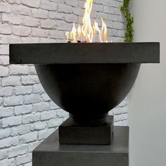 a fire pit sitting on top of a cement block in front of a brick wall