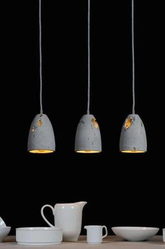 three concrete pendant lights hanging over a dining room table with white dishes and cups on it