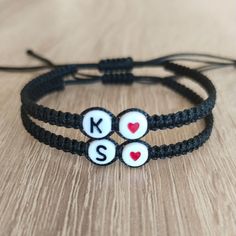 two black string bracelets with white letters and hearts