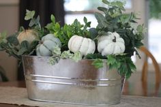 a metal bucket filled with white pumpkins and greenery