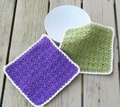 two crocheted dishcloths sitting on top of a wooden table next to a white plate