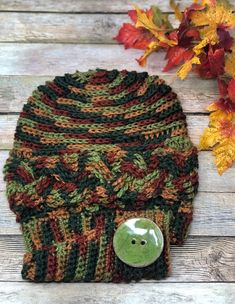 a knitted hat with a green button on the front and brown, orange, and green stripes