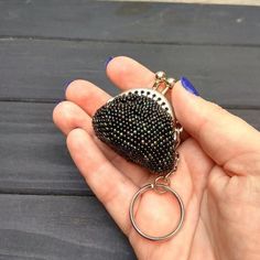 a hand holding a black beaded purse keychain on top of a wooden table