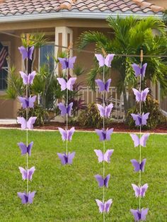 purple paper flowers in front of a house with palm trees and bushes behind them on the lawn