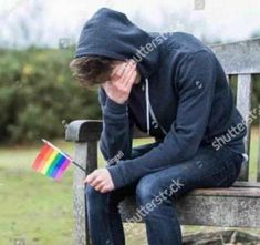 a man sitting on a bench with his head in his hands, holding a rainbow flag