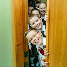 two young boys are peeking out from behind a door with their arms around each other