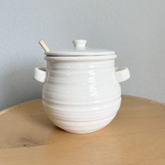 a white ceramic container with a wooden stick sticking out of it's lid on a table