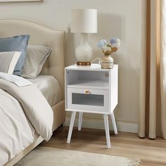 a white nightstand sitting on top of a bed next to a window