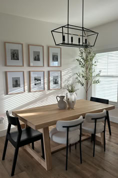 a dining room table with four chairs and pictures on the wall behind it, along with two vases filled with flowers