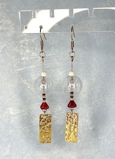 two pairs of earrings with gold and red beads hanging from hooks on a white background