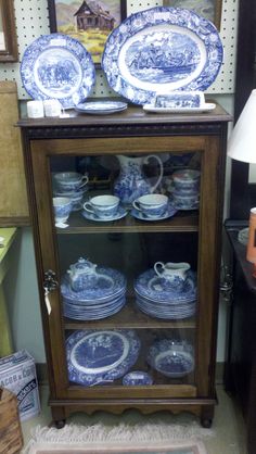 blue and white china cabinet with plates on it in a store display case next to a lamp