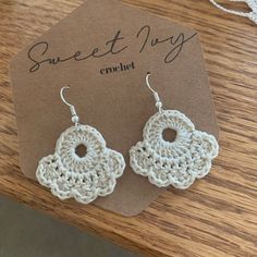 a pair of crochet earrings sitting on top of a wooden table next to a tag