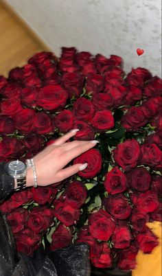 a woman's hand on top of a large bouquet of red roses