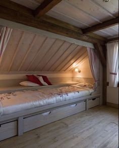 an attic bedroom with two beds and storage drawers under the bed, in front of a window