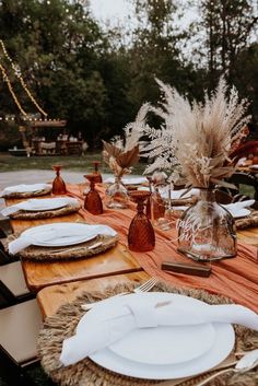 an outdoor table set with plates, napkins and vases for dinner guests to enjoy