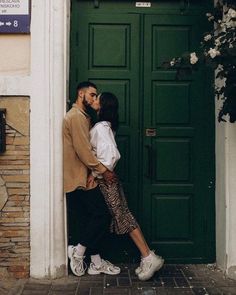 a man and woman kissing in front of a green door