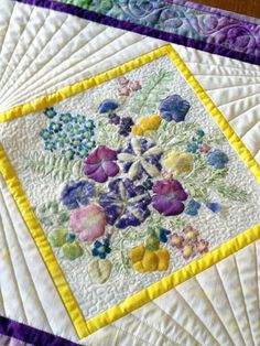 a quilted table topper with colorful flowers on it's edges and yellow border