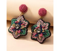 a pair of pink and green beaded flower earrings on top of a white pillow