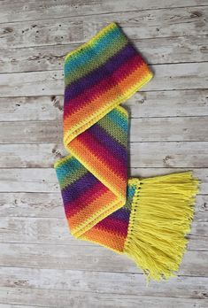 a multicolored knitted scarf with tassels laying on top of a wooden floor