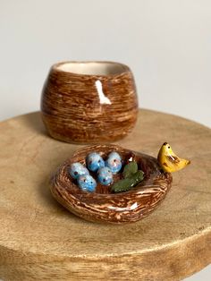 a small ceramic bird nest with blue eggs in it on a wooden stand next to a yellow banana