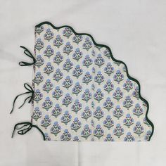 a white cloth with blue flowers on it and green trimming around the edges, sitting on top of a table